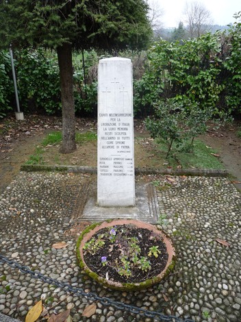 Cippo commemorativo dedicato ai caduti partigiani, situato in un giardino con fiori circostanti.