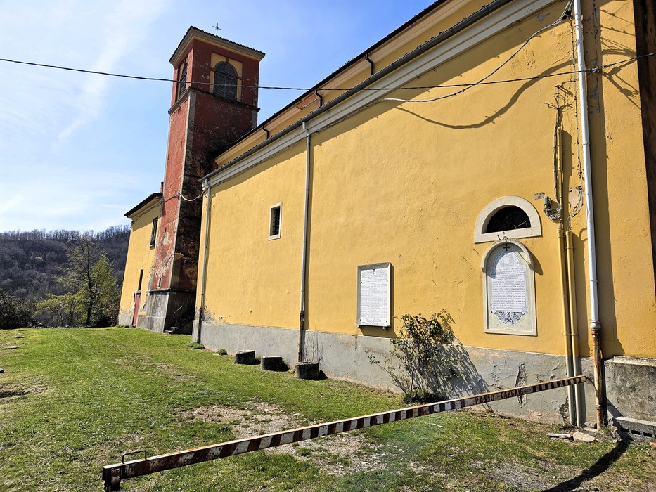 Facciata di chiesa con campanile in mattoni, lapide con iscrizione sotto una finestra ad arco.