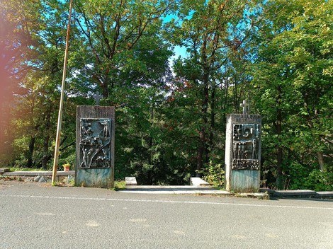 Memoriale dei caduti della Benedicta, con sculture affiancate da alberi e sentiero sottostante.