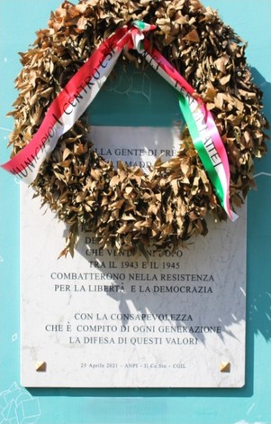 Lapide commemorativa dedicata agli antifascisti e partigiani, adornata con una corona di foglie e nastri tricolori.