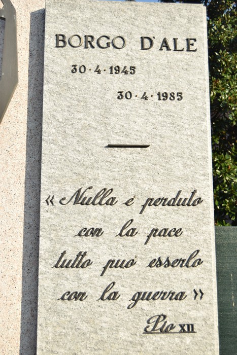 Lapide in pietra con iscrizione dedicata a Borgo d'Ale, sormontata da una linea decorativa e citazione finale.