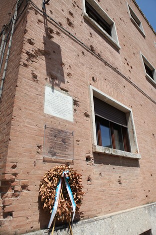 Lapide commemorativa con targa, decorata con una corona di alloro, su un edificio a Folloni.