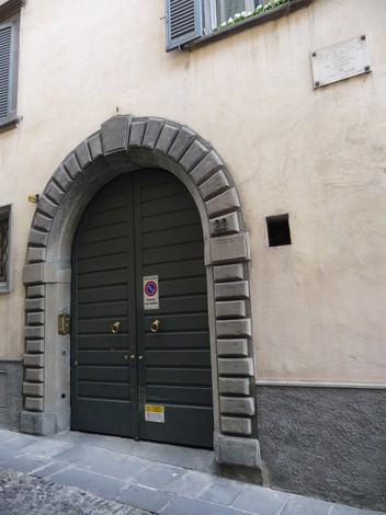 Ingresso di un edificio storico con una grande porta verde e una lapide murale affissa sopra.