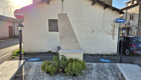 Monumento al Campo PG54 con iscrizioni, situato in un'area urbana con lampioni e vegetazione.