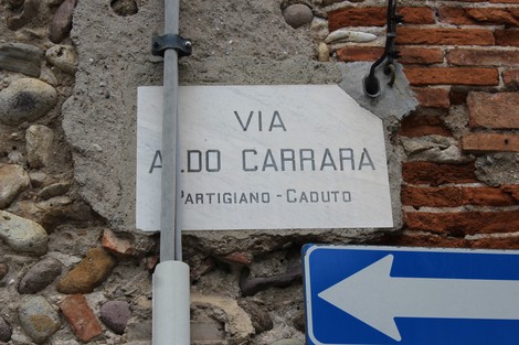 Targa stradale in marmo con l'indicazione della via Aldo Carrara, in un contesto di muratura storica.
