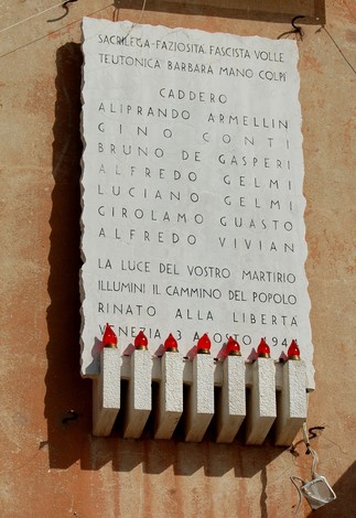 Lapide commemorativa per i fucilati Vivian, Armellini, Conti e altri, con candele accese in ricordo.