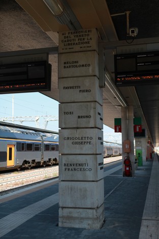 Monumento dedicato ai ferrovieri caduti per la libertà, con nomi incisi su un pilastro in una stazione ferroviaria.