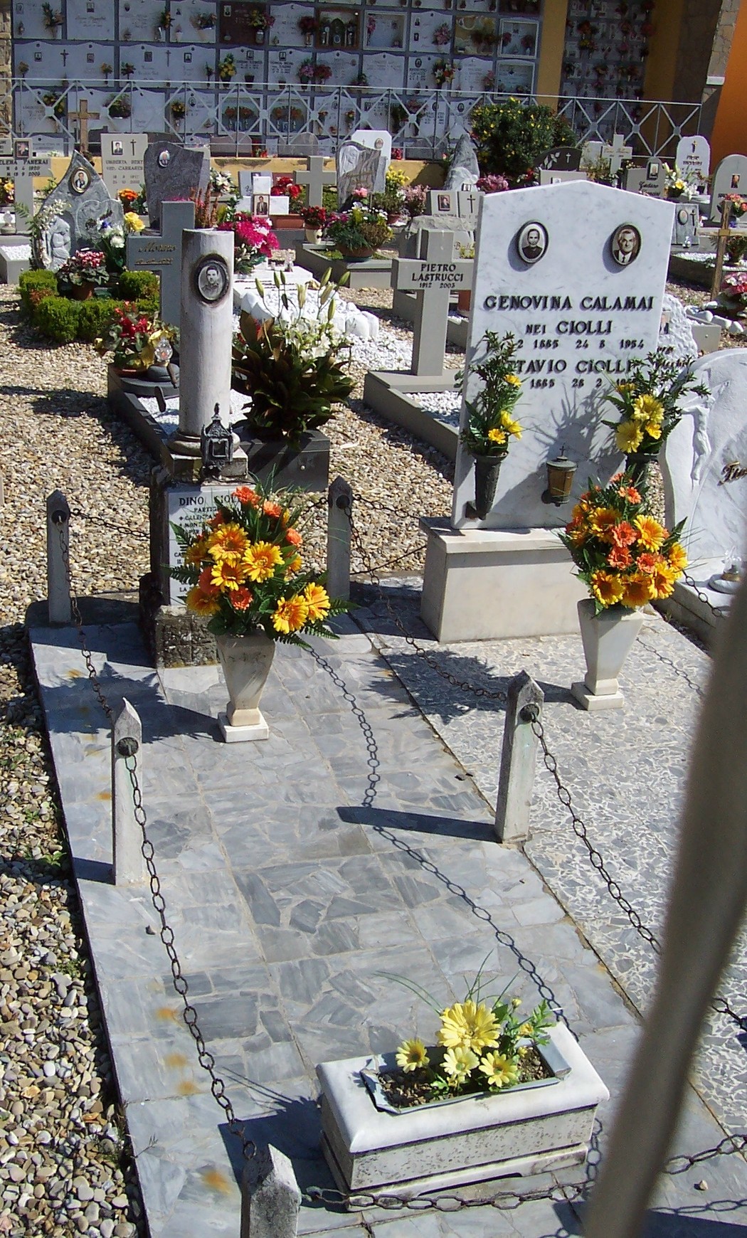 Sepolcro di Ciolli, ornato da fiori e candele, in un cimitero ben curato e suggestivo.