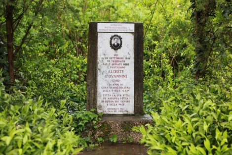 Cippo commemorativo dedicato a Alceste Giovannini, immerso nel verde, con inscriptioe a lui dedicata.