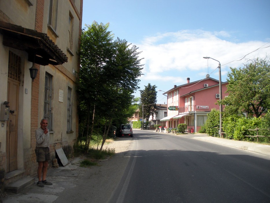 Immagine di una strada a Allieri, con edifici e vegetazione circostante in una giornata soleggiata.