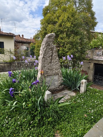 Monumento a Boldi e Innocenti circondato da fiori, con un'architettura rustica e un cielo nuvoloso.