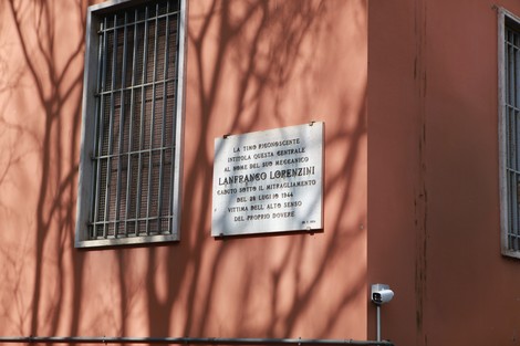Lapide commemorativa dedicata a Lanfanto Lorenzini, su edificio con parete arancione e finestre con inferriate.