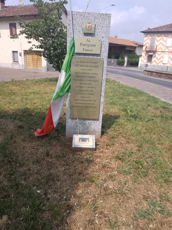 Monumento ai partigiani, composto da una stele e una bandiera italiana, situato in una zona verde.