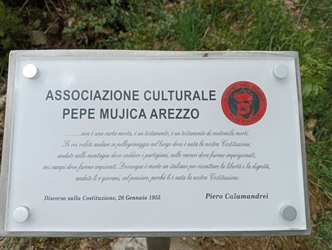 Cippo commemorativo dedicato a Pepe Mujica, immerso nella natura e circondato da vegetazione.