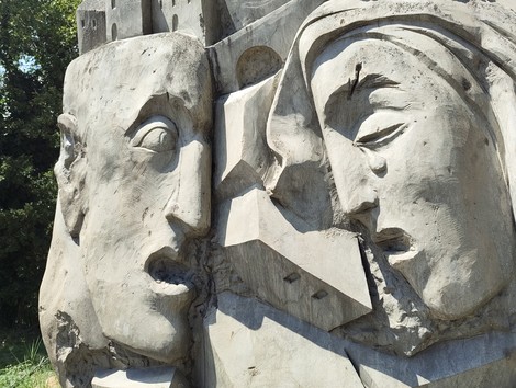Dettaglio scultoreo in pietra del Monumento alla Libertà, con due volti umani scolpiti ad alto rilievo.