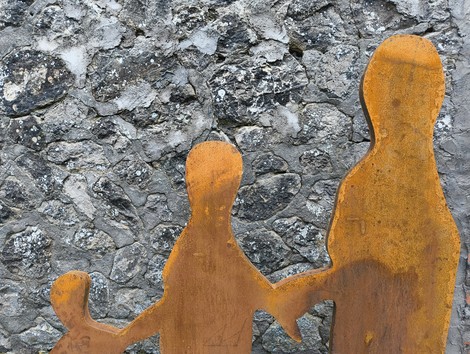 Silhouette di figure umane in metallo, su sfondo di pietra, che rappresentano il "Percorso per Fornasini".