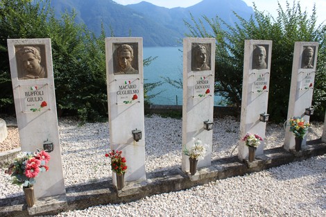 Sacrario dei Tredici Martiri, monumento commemorativo con ritratti e decorazioni floreali sullo sfondo lacustre.