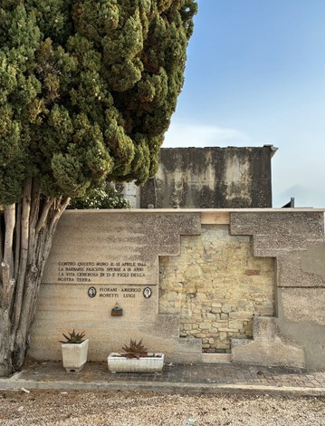 Memoriale commemorativo a Fiorani e Moretti, con elementi decorativi e una parete di pietra.