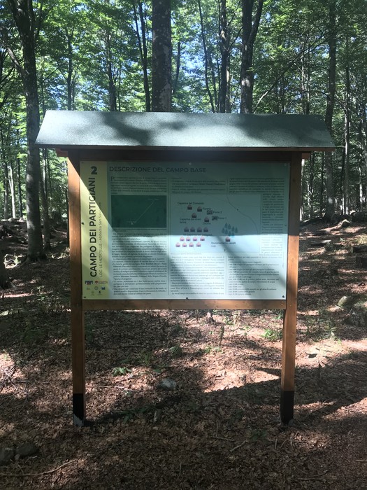 Campo del 7° battaglione "Ovidio Sabatini", immerso nel verde, con pannello informativo sulla storia del battaglione.
