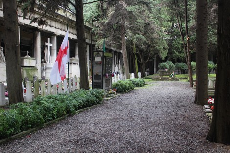 Il sepolcro di Poletaev in un cimitero, con bandiera e sentiero circondato da alberi e tombe.