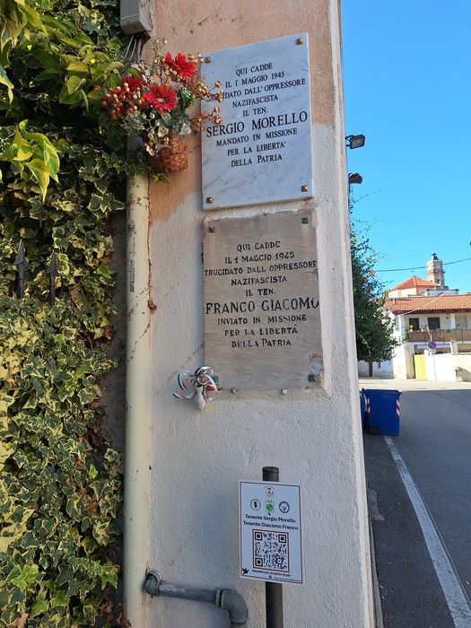 Due lapidi marmoree con iscrizioni affiancate su una parete esterna, sopra un cartello informativo.