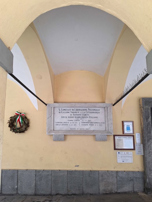Lapide commemorativa dedicata ai patrioti, situata in un'area architettonica storica.