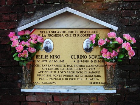 Targa commemorativa dedicata a Beilis e Curino, con fiori artificiali e iscrizioni di memoria.