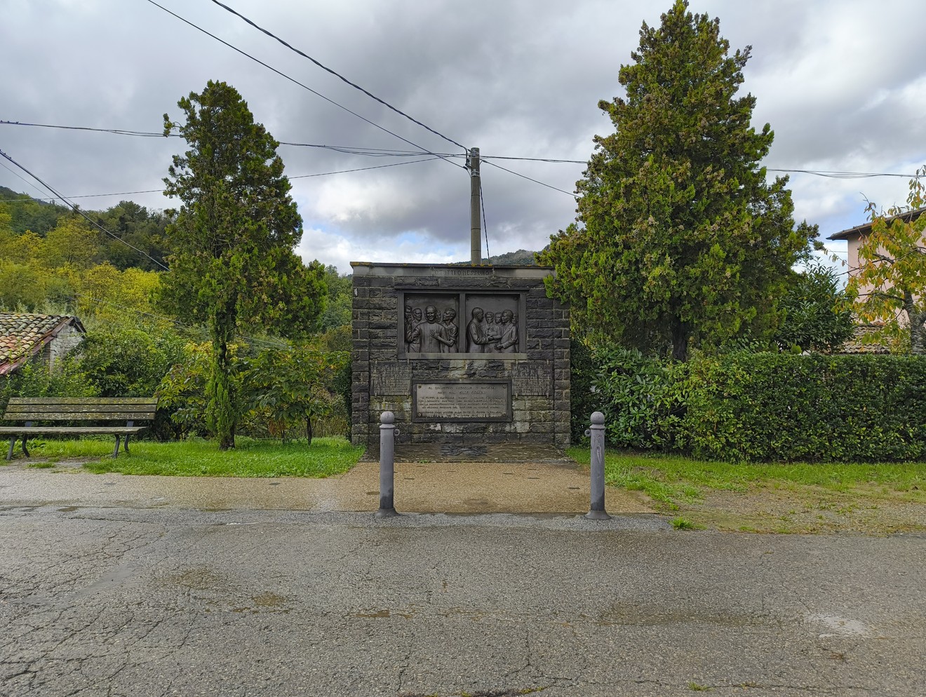 Monumento a Comini, un’opera commemorativa immersa nella natura con pannelli decorativi e vegetazione circostante.