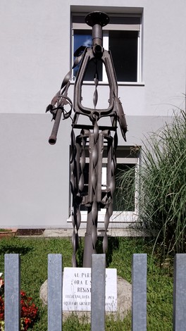 Monumento al partigiano, scultura in metallo che rappresenta un combattente della Resistenza, sullo sfondo di un edificio.
