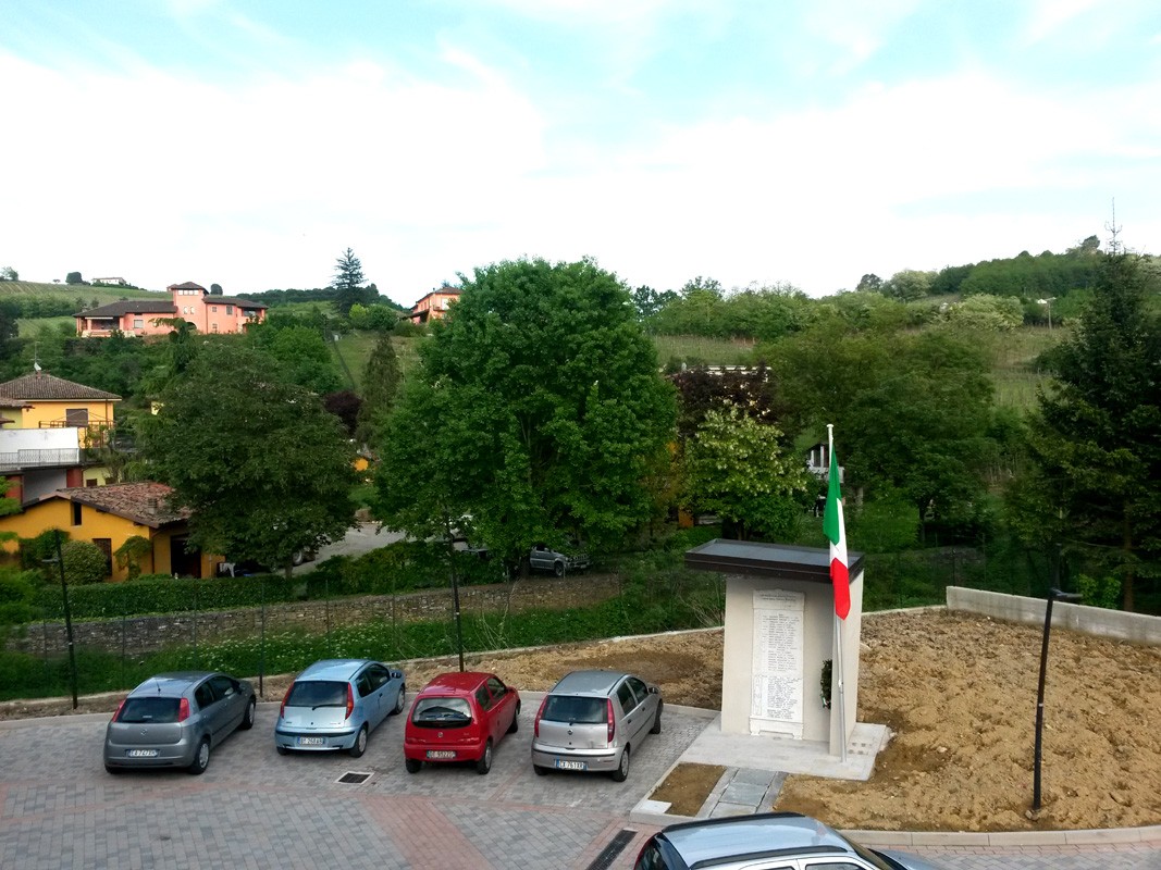 Monumento ai caduti di Torricella Verzate, circondato da verde e auto, simbolo di memoria e rispetto.