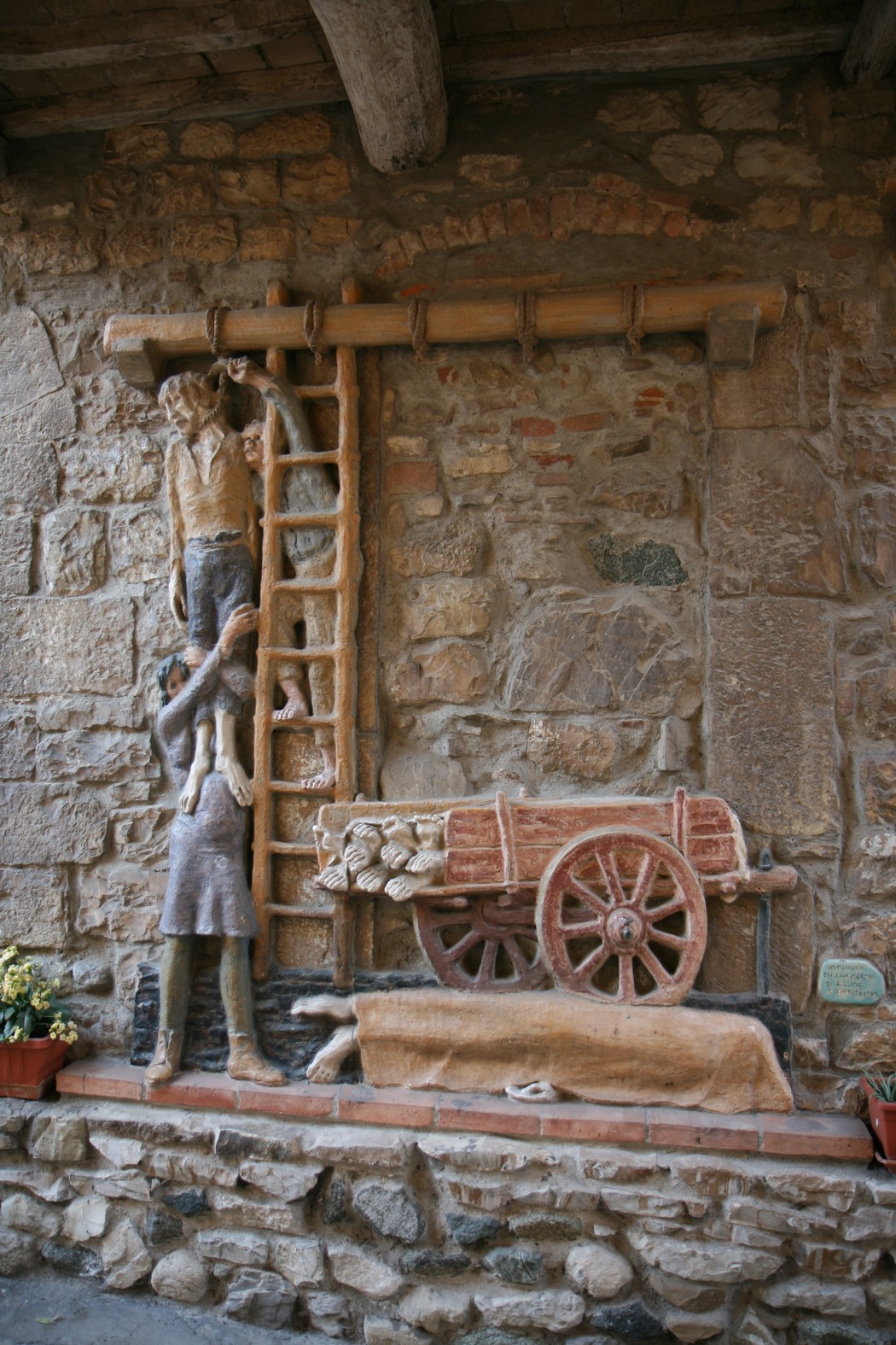 Bassorilievo che commemora i martiri di Figline con figure umane e un carretto tradizionale.
