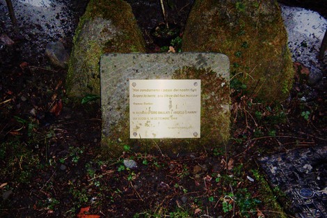Cippo commemorativo dedicato a Ballati e Giannini, immerso nella vegetazione.