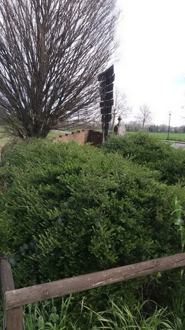 Cippo commemorativo dedicato ai partigiani di Camuzzago circondato da cespugli e vegetazione.