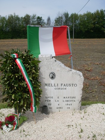 Cippo commemorativo dedicato a Fausto Melli, eroe e martire per la libertà, con decorazioni e bandiera italiana.