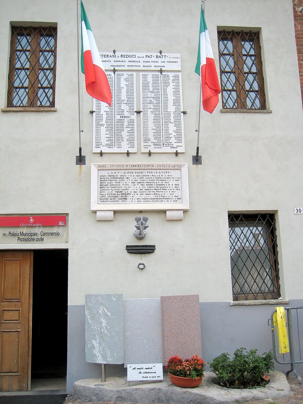 Monumento ai caduti con elenco dei nomi e bandiere, situato su una facciata di edificio pubblico.