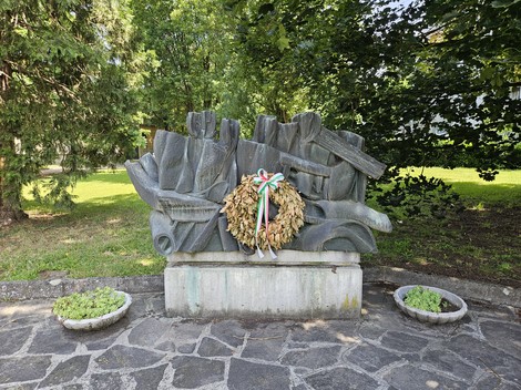 Monumento alla Resistenza con corona di fiori, circondato da verde, in un contesto di commemorazione.