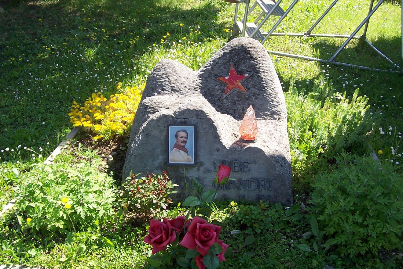 Sepolcro di Ciandri, decorato con fiori, una foto e simboli su una pietra in un ambiente sereno.