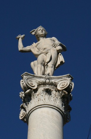 Statua di Mercurio su colonna decorata, simbolo del commercio e della comunicazione. Sfondo blu.