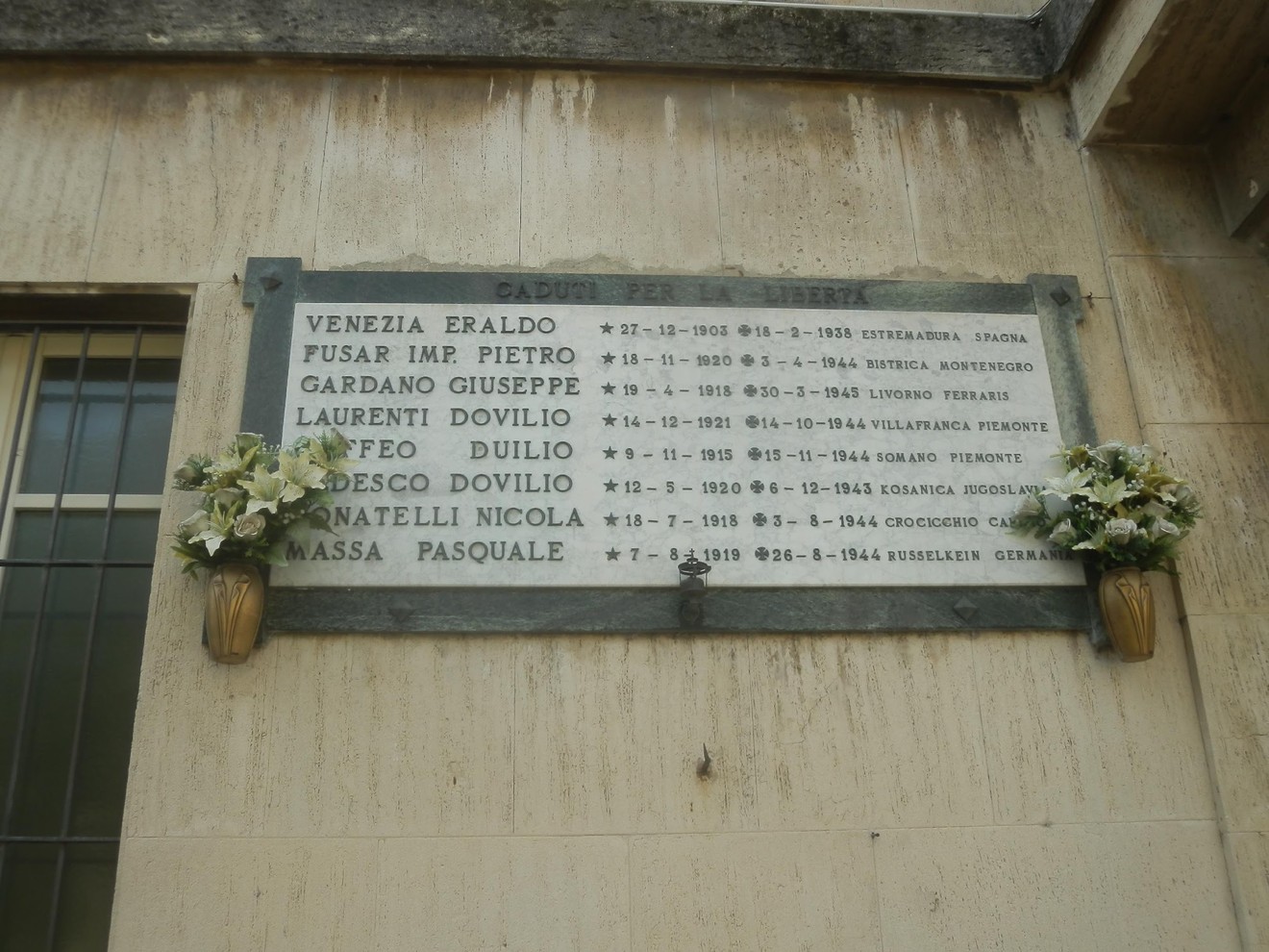 Lapide commemorativa ai caduti per la libertà, con elenchi di nomi e date di partecipazione ai conflitti.