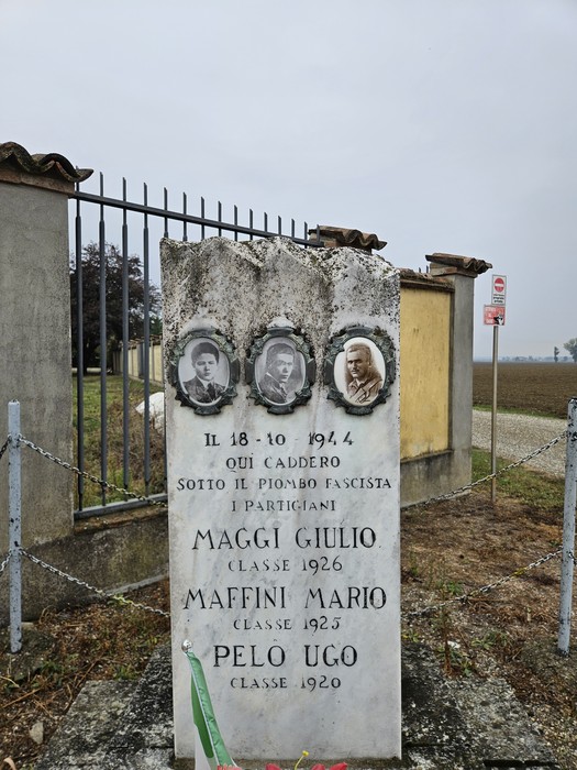 Cippo in pietra con tre ritratti ovali e iscrizione, dietro una cancellata di ferro.