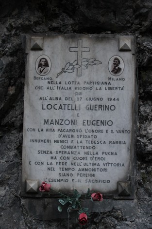 Lapide commemorativa dedicata a Locatelli e Manzoni, con simboli e decorazioni floreali.
