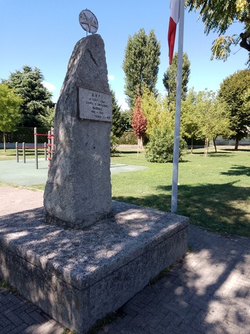 Monumento alla Liberazione, pietra grigia con iscrizioni, immerso in un parco con alberi e aree verdi.