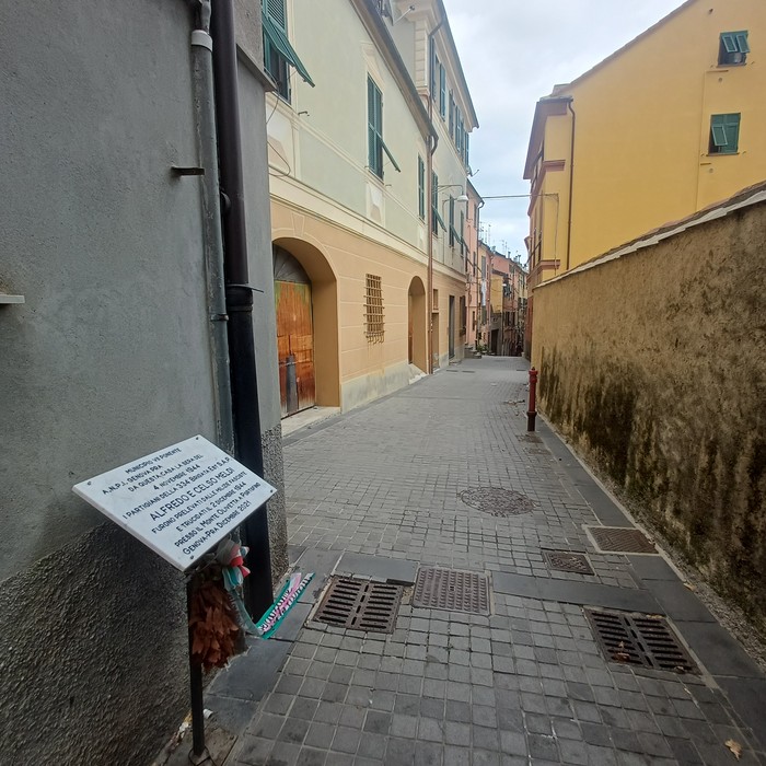 Lapide con iscrizione su una parete, all'ingresso di un vicolo tra edifici di un centro storico.
