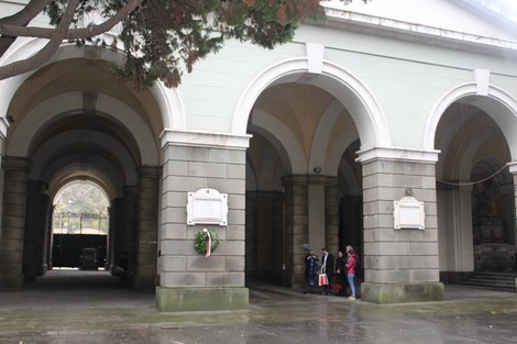 Lapide commemorativa in un edificio storico, con visitatori che si soffermano in un ambiente sobrio e contemplativo.