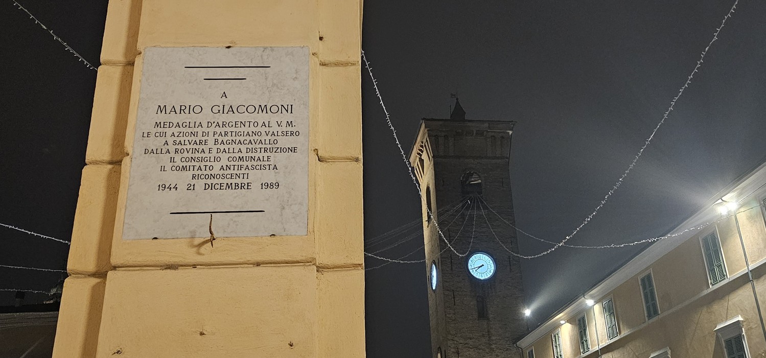 Lapide commemorativa dedicata a Mario Giacomoni, situata in un contesto urbano.