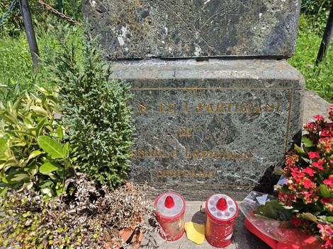 Cippo commemorativo con fiori e candele, dedicato ai partecipanti di un evento storico.