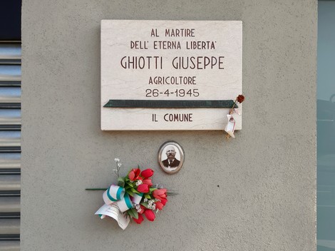 Lapide commemorativa di Giuseppe Ghiotti, martire per la libertà, con fiori e foto.