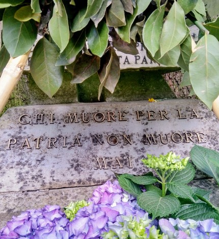 Cippo commemorativo con lastre di pietra e fiori, dedicato ai caduti per la patria.