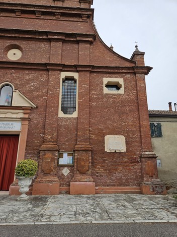 Lapide commemorativa su un muro di mattoni rossi, collocata accanto a una chiesa storica.