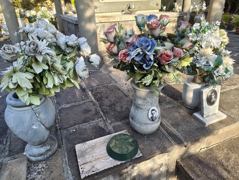 Sacrario ai caduti con vasi di fiori artificiali e pietre commemorative in un ambiente sacro e tranquillo.